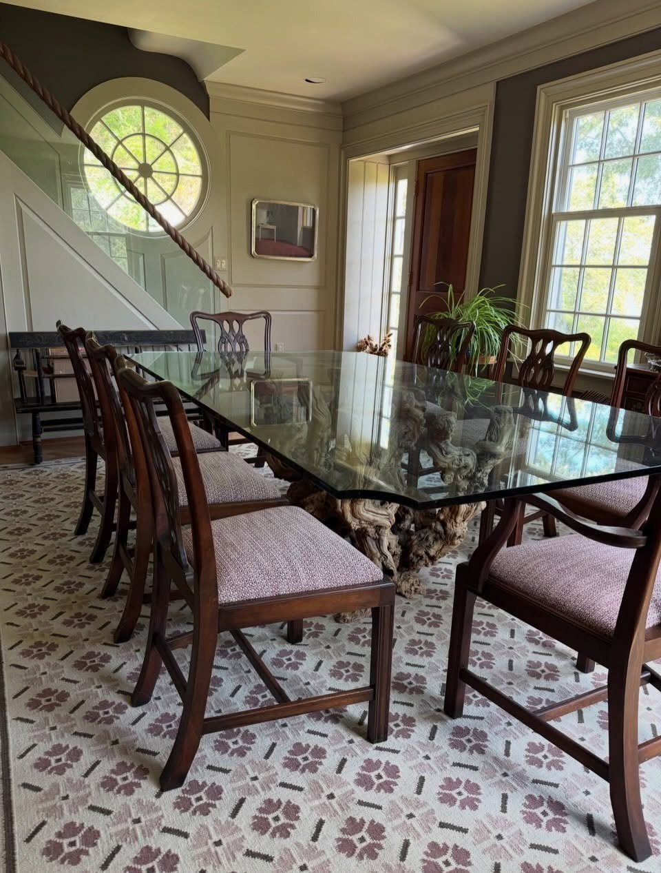 Glass-top dining table and wooden chairs on a large floral patterned area rug.