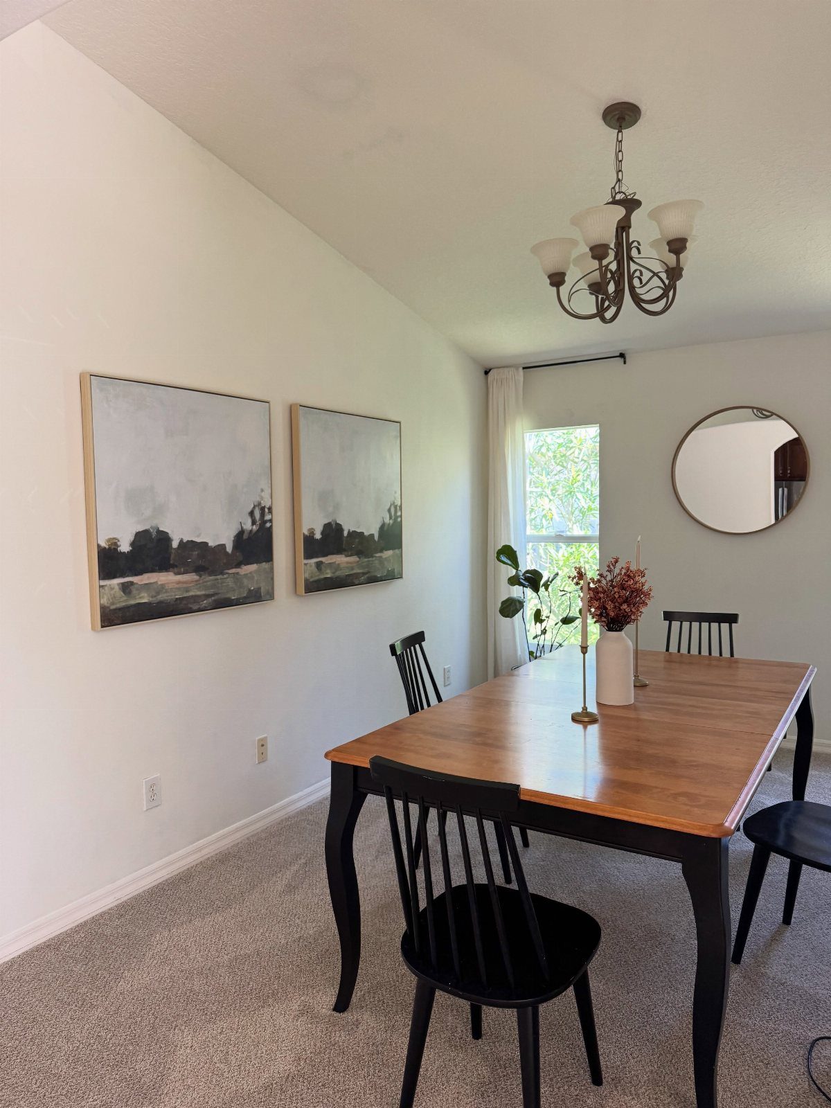 Dining room with a wooden table, black chairs, and grey wall-to-wall carpeting.