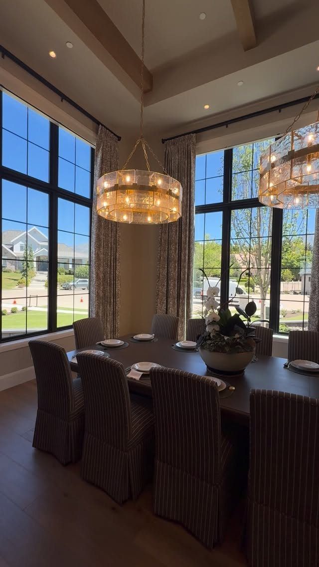 Two gold drum chandeliers hanging over a dark wood dining table with striped chairs.