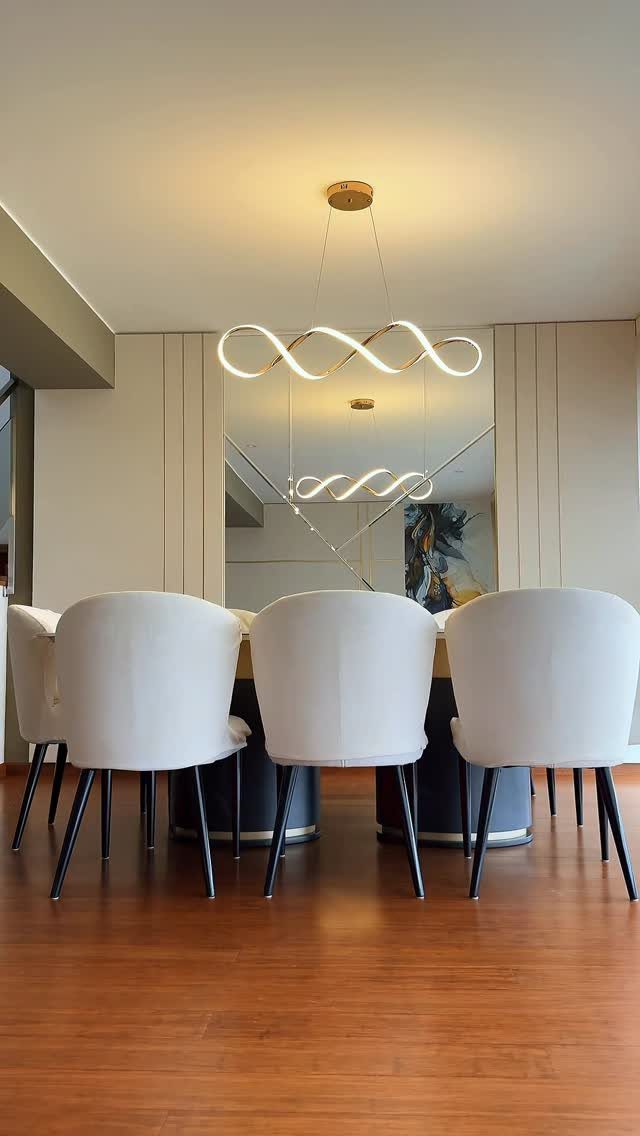 Wavy gold LED chandelier hanging over a dining table with white chairs.