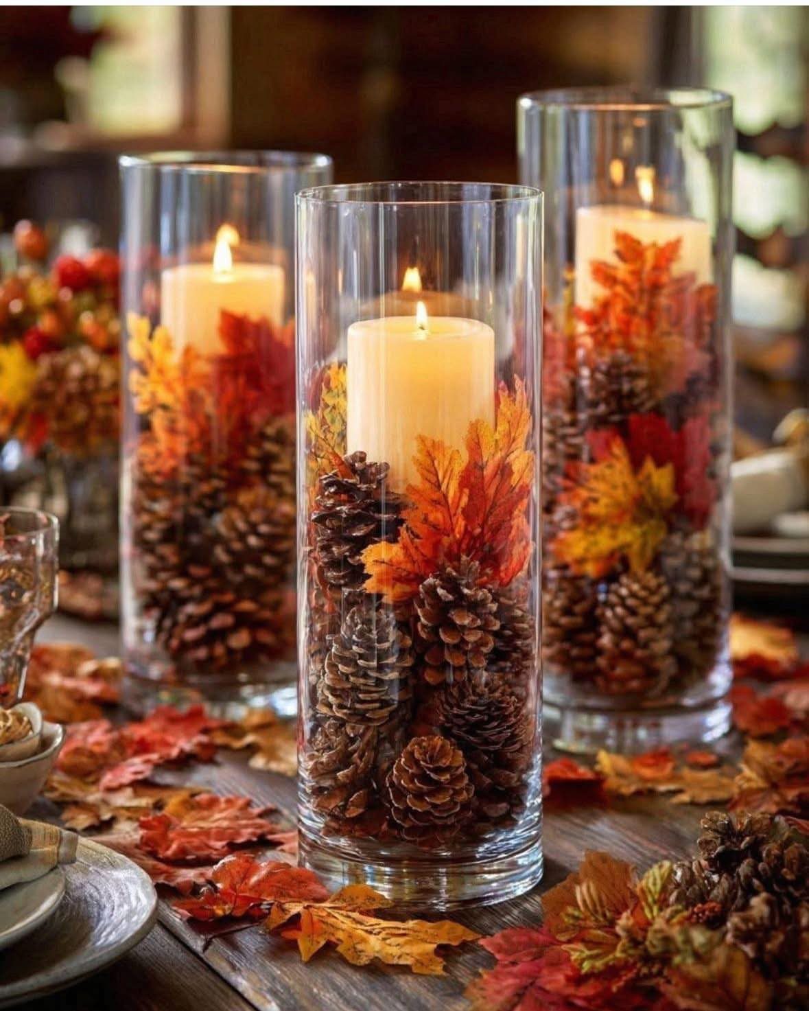 Autumn centerpiece with candles, pinecones, and orange leaves on a rustic wood table.