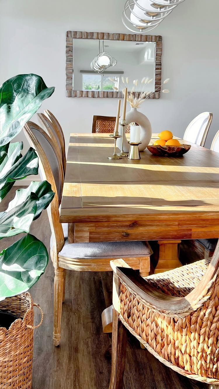 Wooden dining table decorated with white candles, a white vase, and orange fruit.