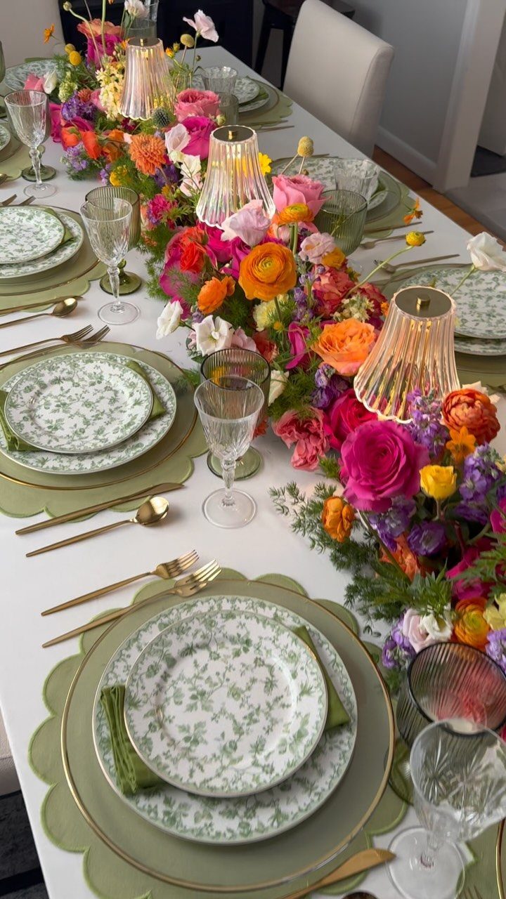 Dining table set with green patterned plates and a colorful floral centerpiece.