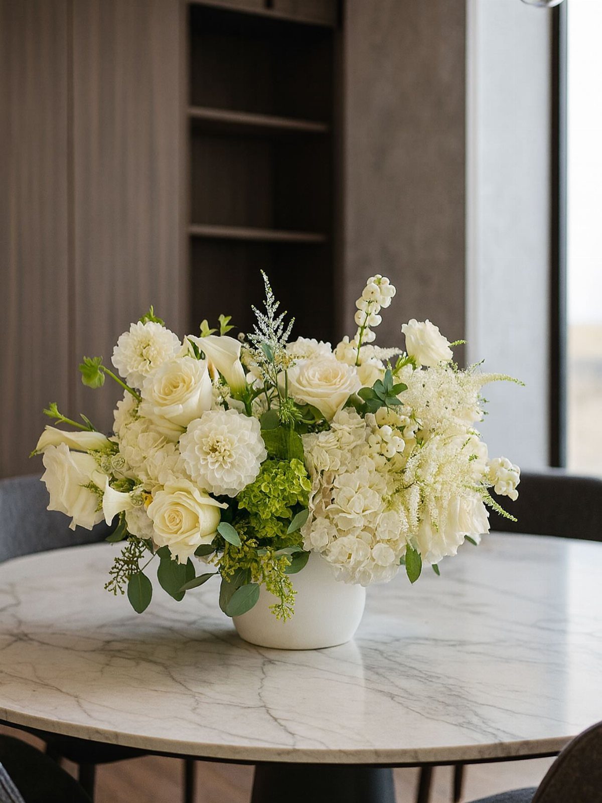 White floral arrangement in a ceramic vase on a white marble dining table.