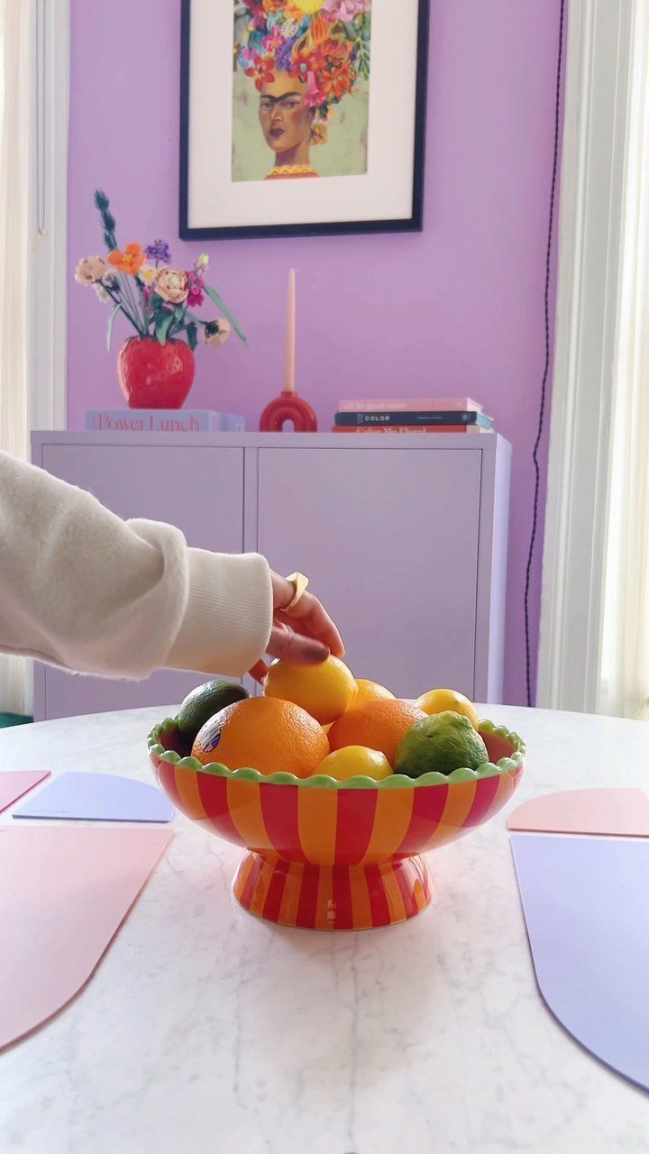 Striped pedestal bowl filled with citrus fruits on a white marble table.