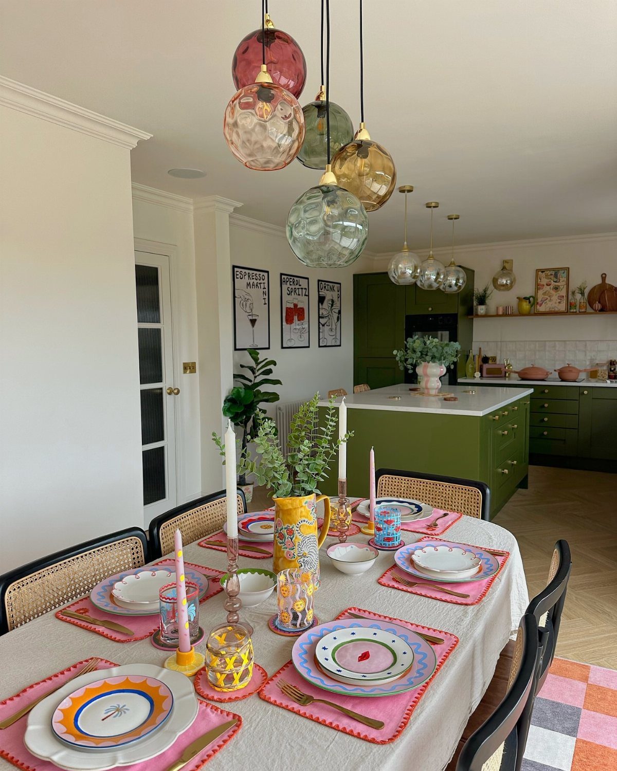 Dining table set with colorful plates, pink placemats, and yellow decorative candles.