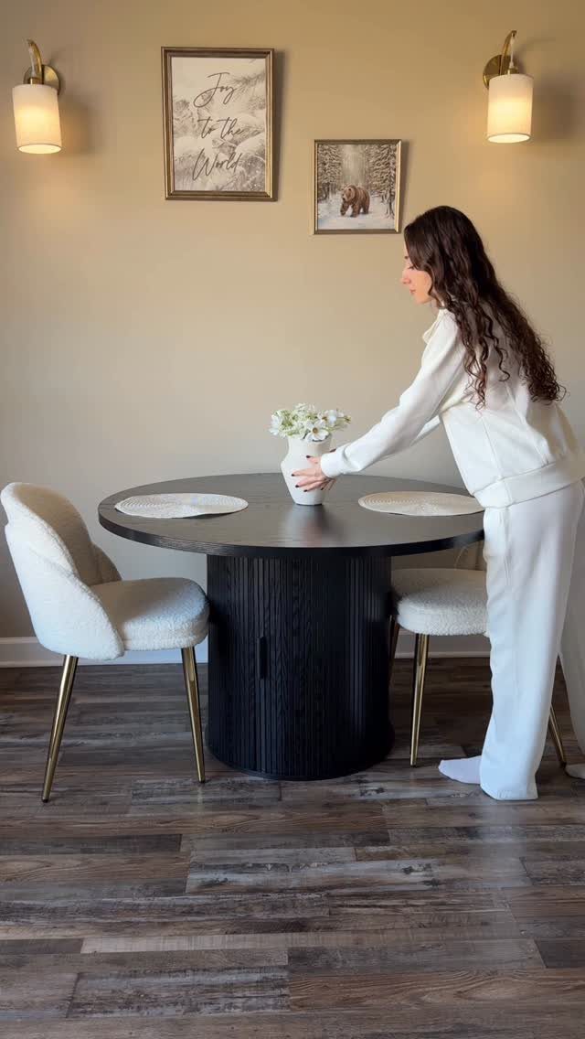 Woman placing flowers on a round black dining table with white chairs.