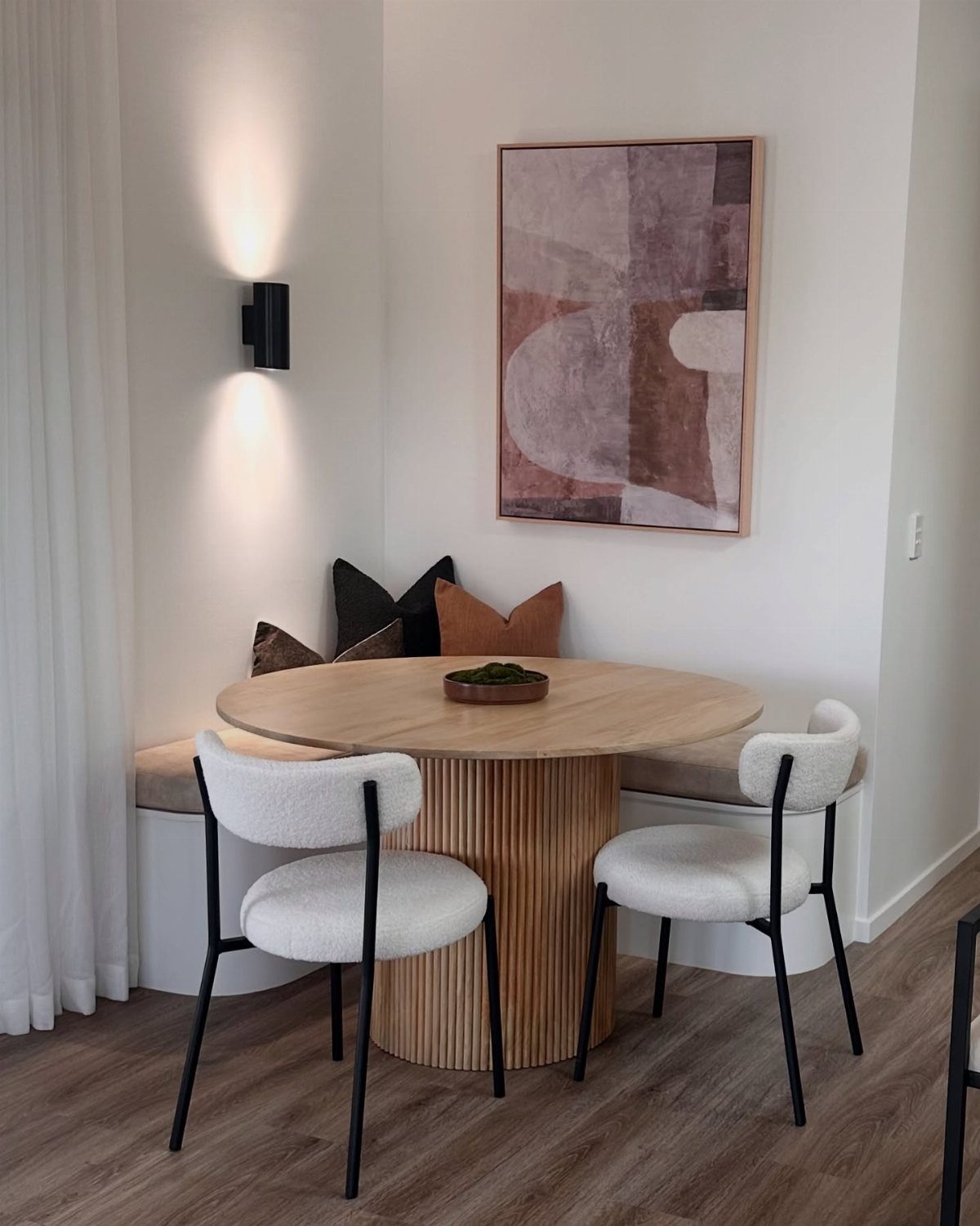 Round wooden dining table with white chairs and built-in corner bench seating.