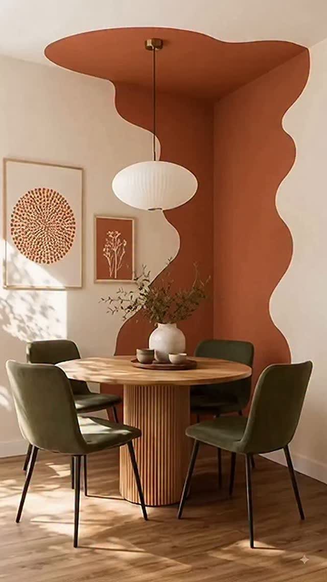 Round wooden dining table with green chairs positioned in a terracotta painted corner.