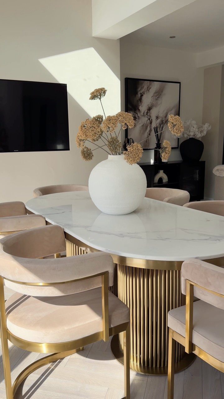 Oval marble dining table with gold base and beige chairs in bright room