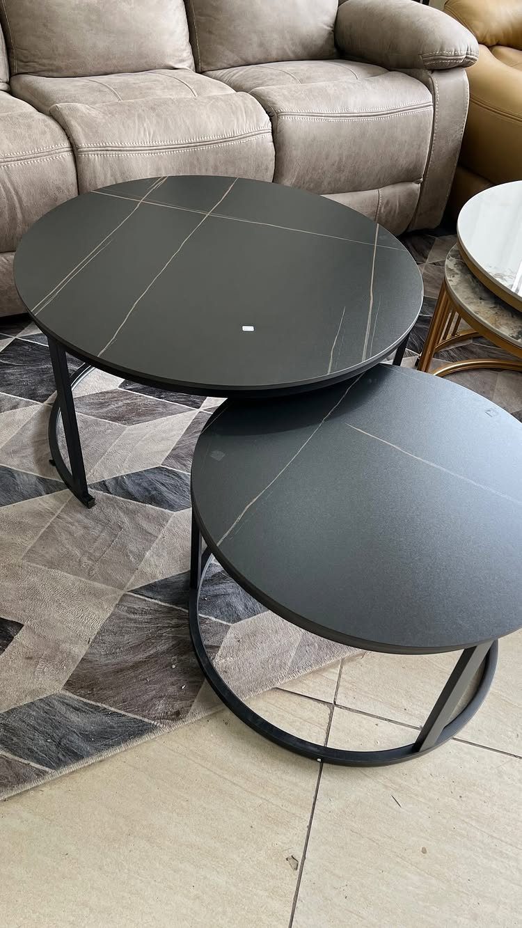 Two black marble-effect nesting coffee tables on a grey geometric rug near a sofa.