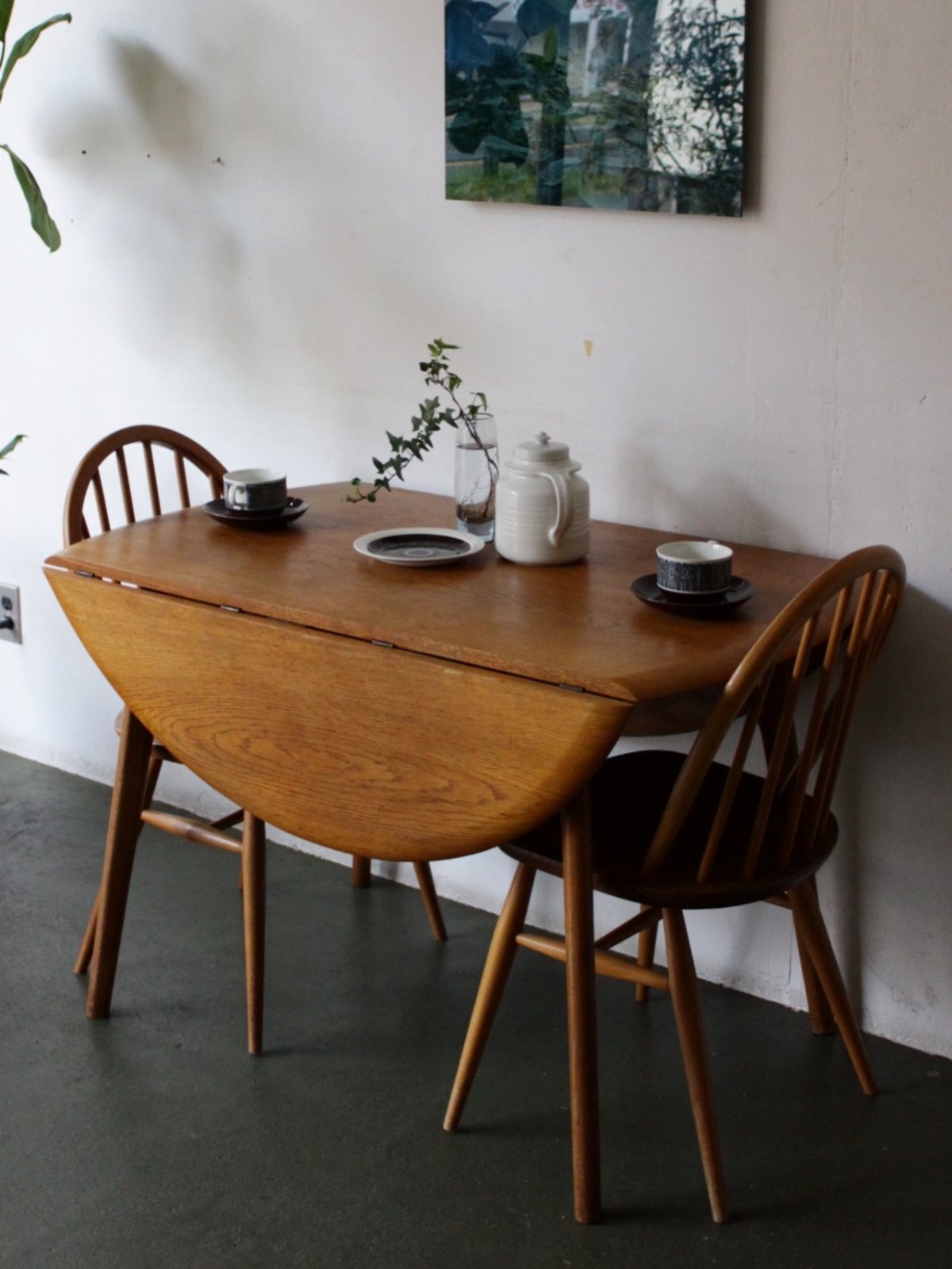 Wooden drop-leaf dining table with two matching chairs against a white wall.