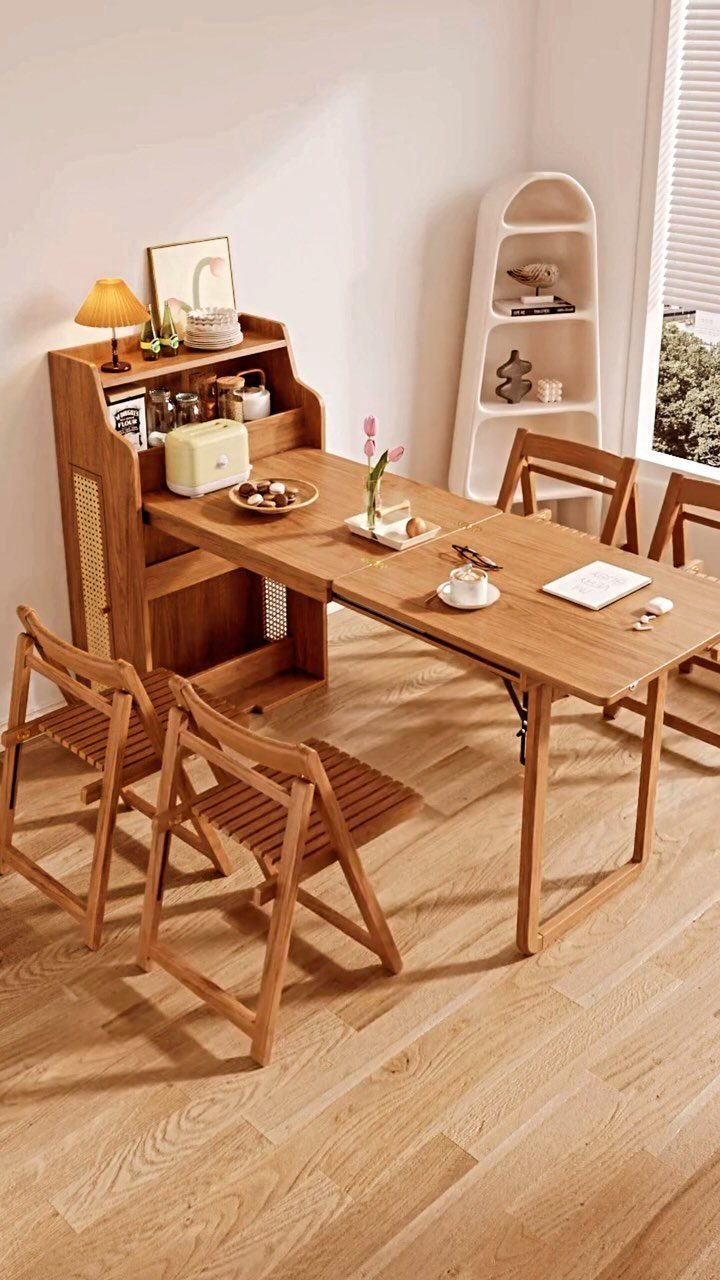 Wooden dining table with folding chairs and attached storage cabinet in a bright room.