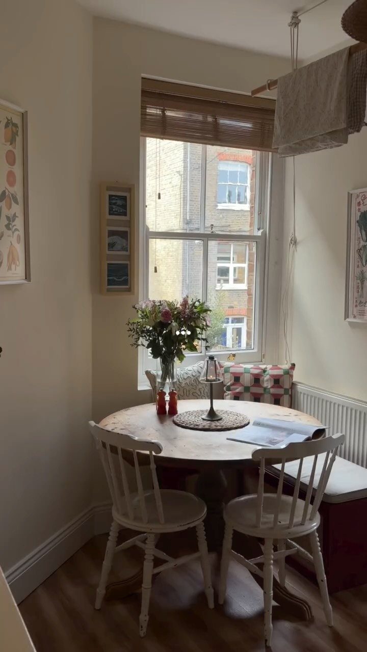 Round wooden dining table with white chairs tucked into a bright room corner.