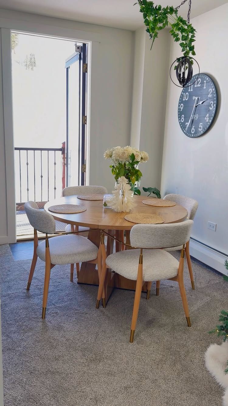Round wooden dining table with grey chairs in a small white room.
