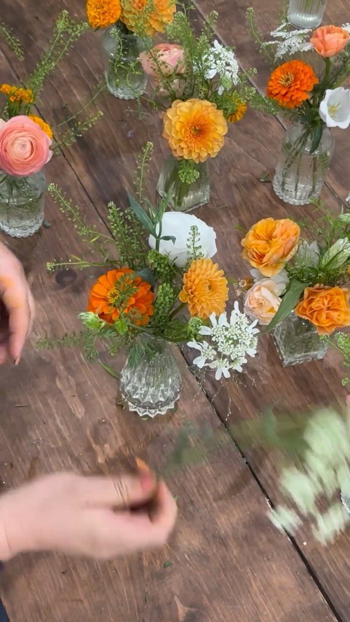 Small glass bud vases with orange and yellow flowers on a wooden table.