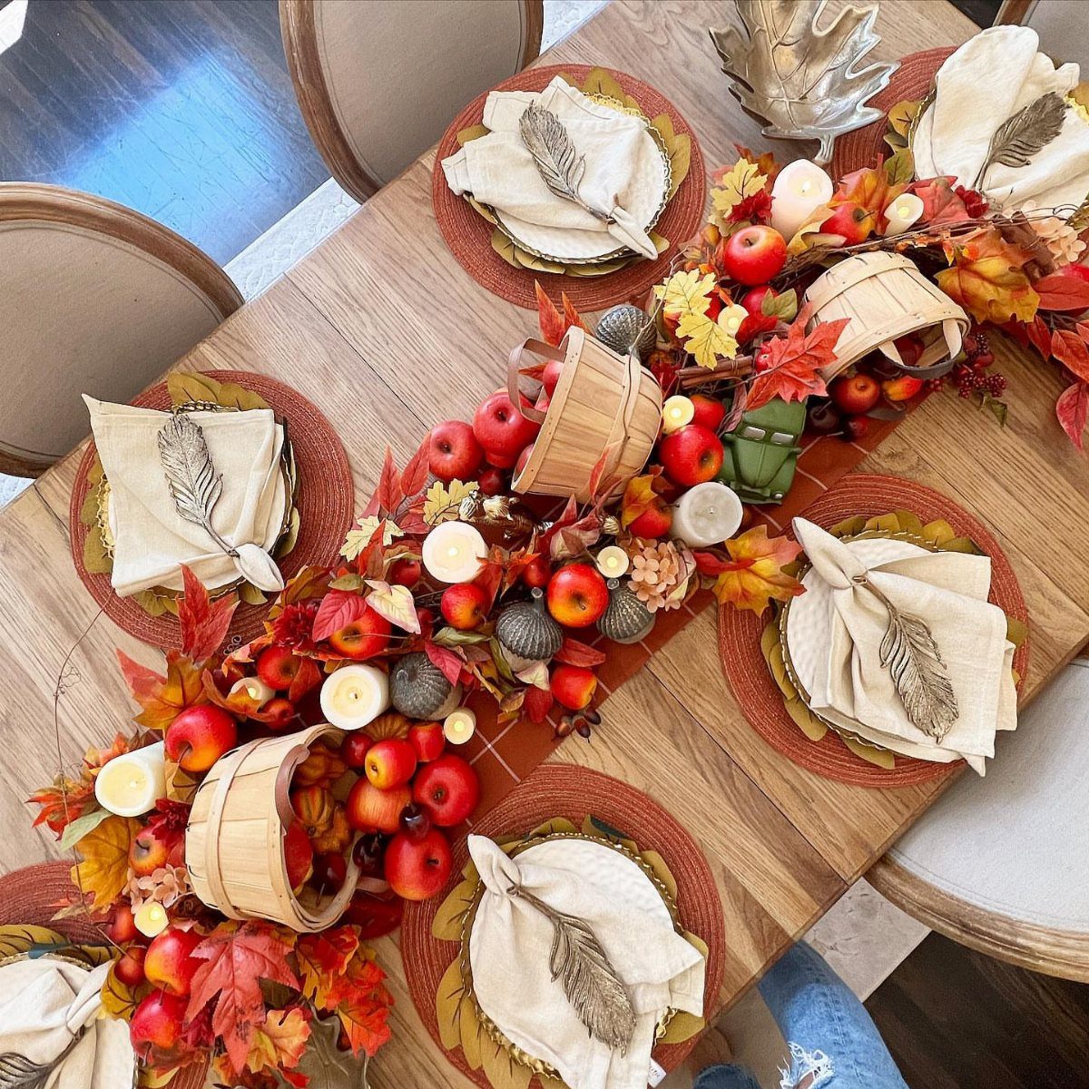 Fall dining table centerpiece featuring red apples, autumn leaves, and rustic baskets.