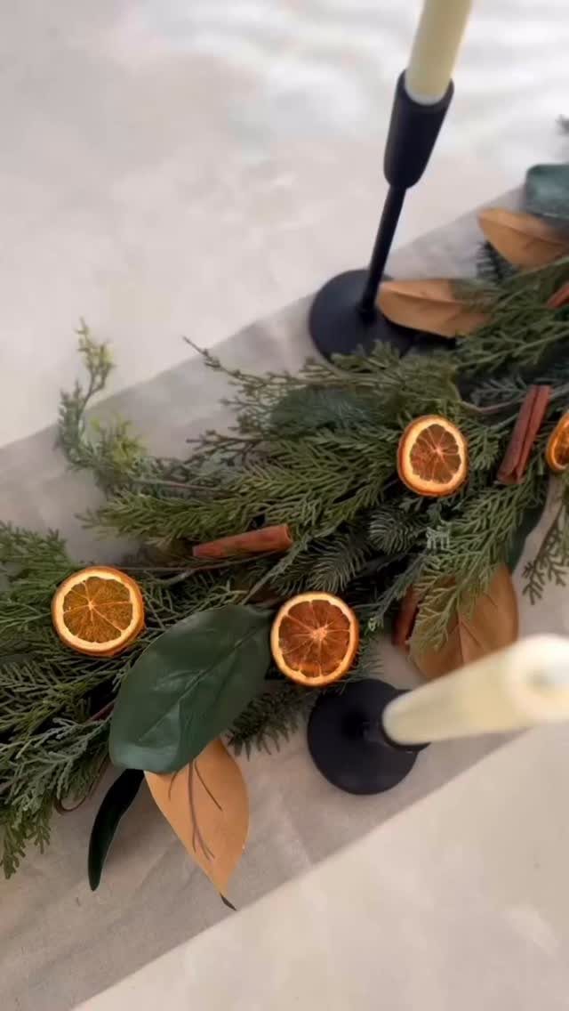 White taper candles in black holders set within a green evergreen table garland.