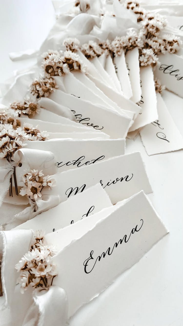 Handwritten calligraphy place cards with dried white flowers and white ribbons on white background
