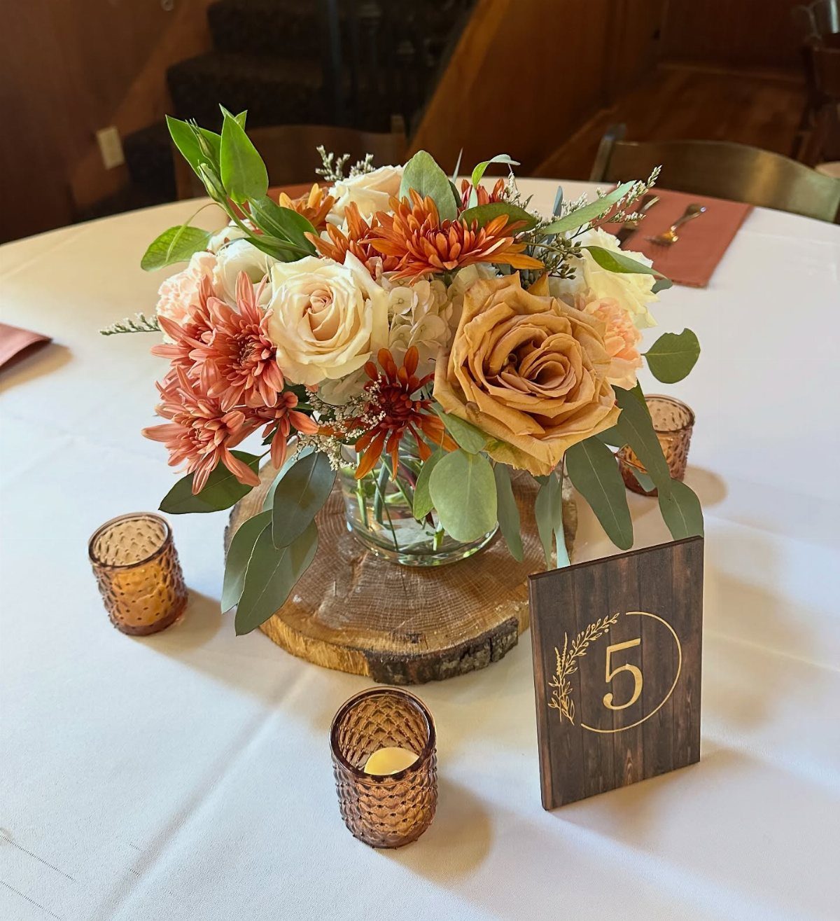 Low floral centerpiece with orange roses on a wooden slice with amber votives.