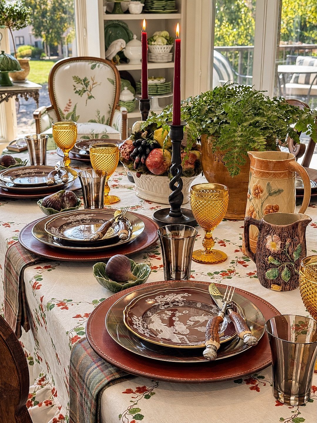Brown patterned plates and amber glasses on a floral tablecloth with fall decor.