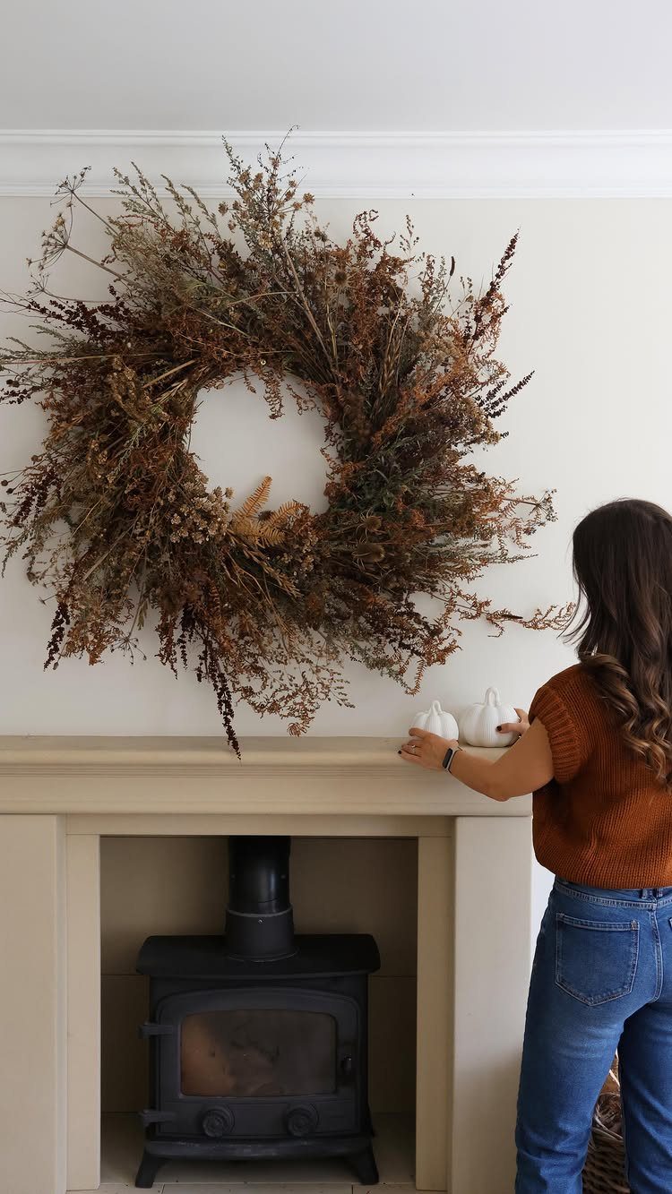 Large dried floral fall wreath hanging above a fireplace mantel with white pumpkins.