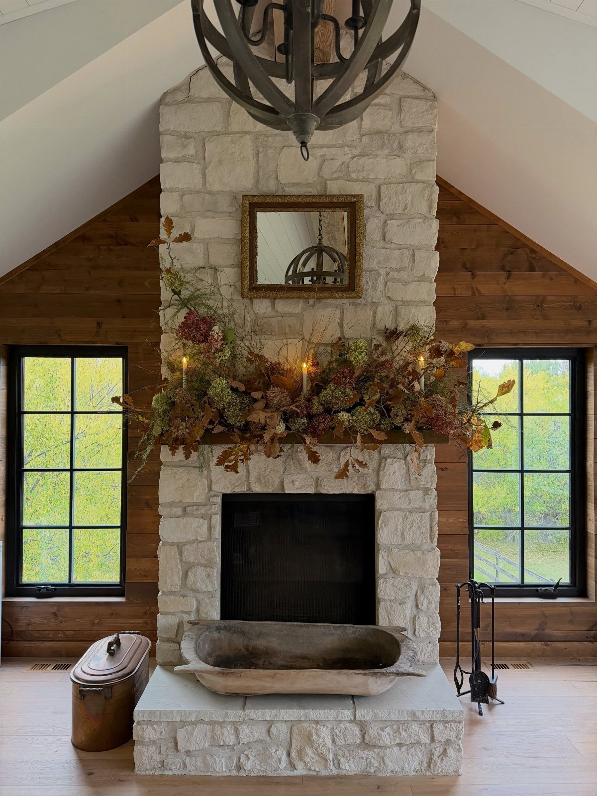 Stone fireplace mantel decorated with organic autumn foliage, branches, and small glowing candles.