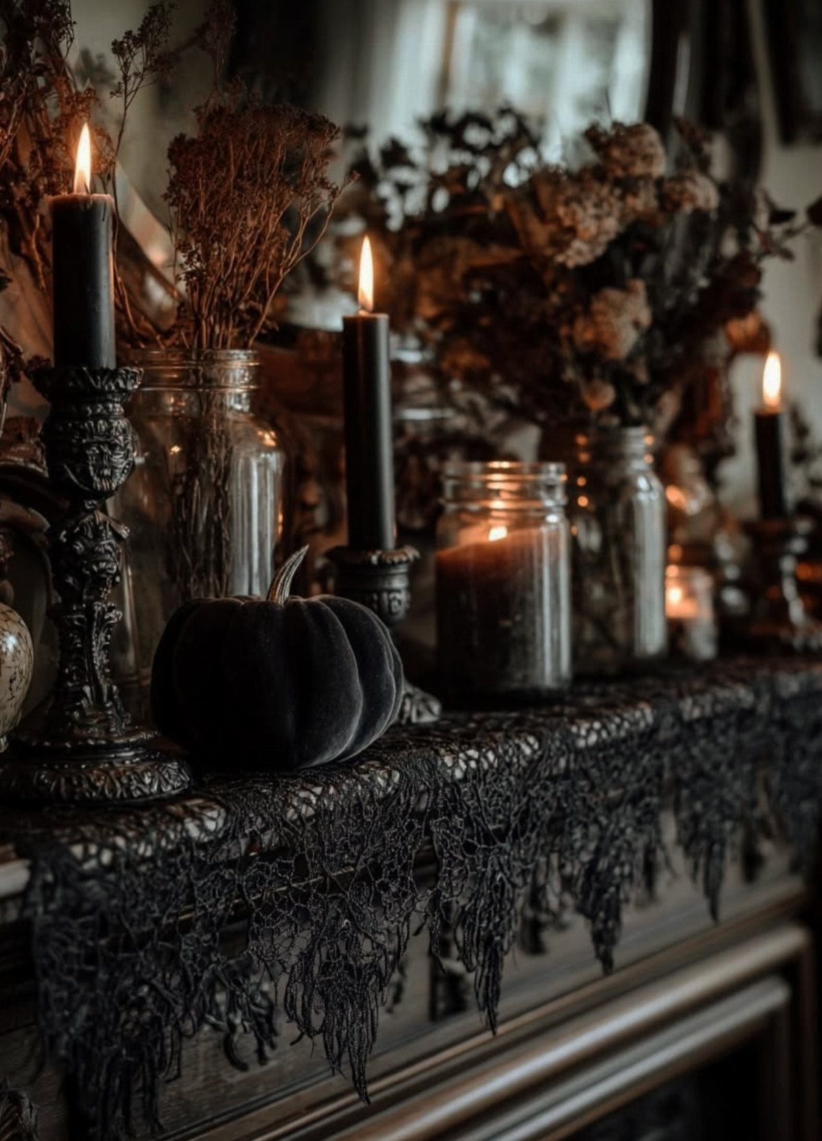 Dark fireplace mantel with black candles, dried flowers, and a black velvet pumpkin.