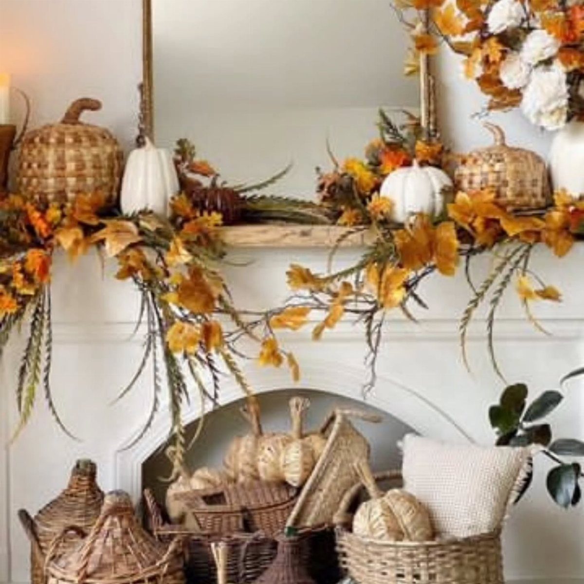 White fireplace mantel decorated with autumn leaf garland, white pumpkins, and wicker accents.