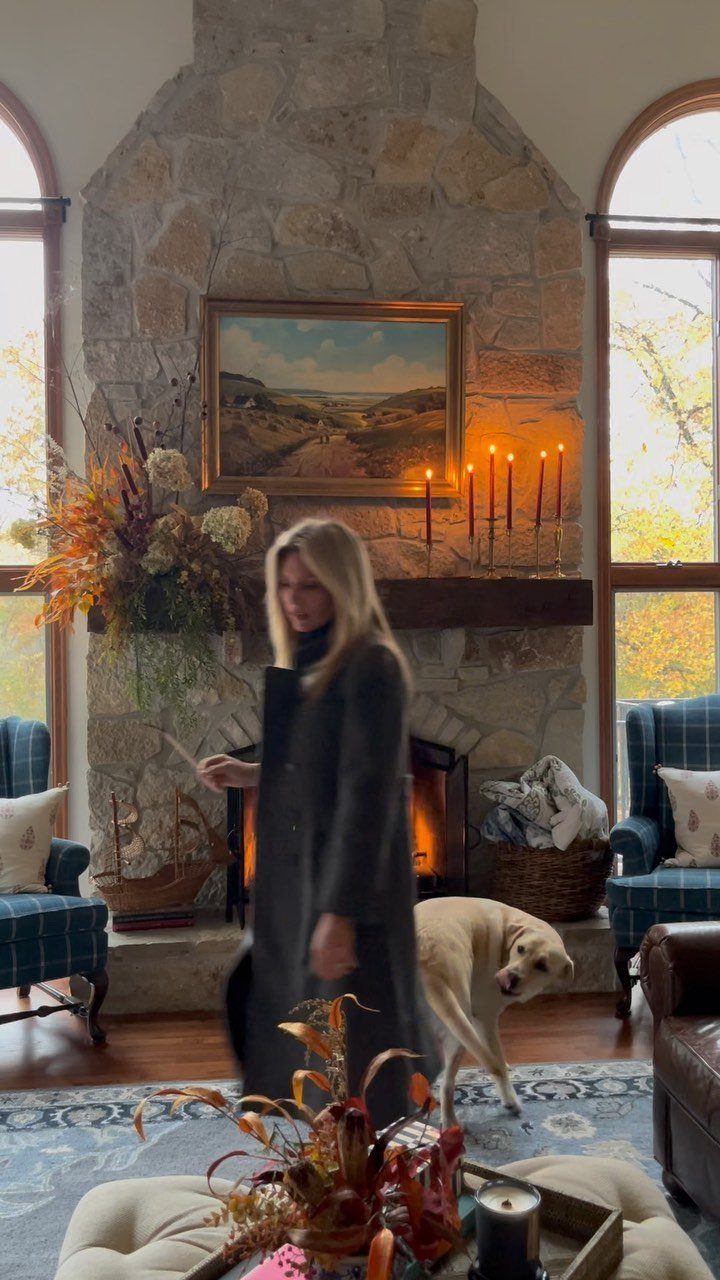 Stone fireplace mantel decorated with autumn leaves and lit orange taper candles.