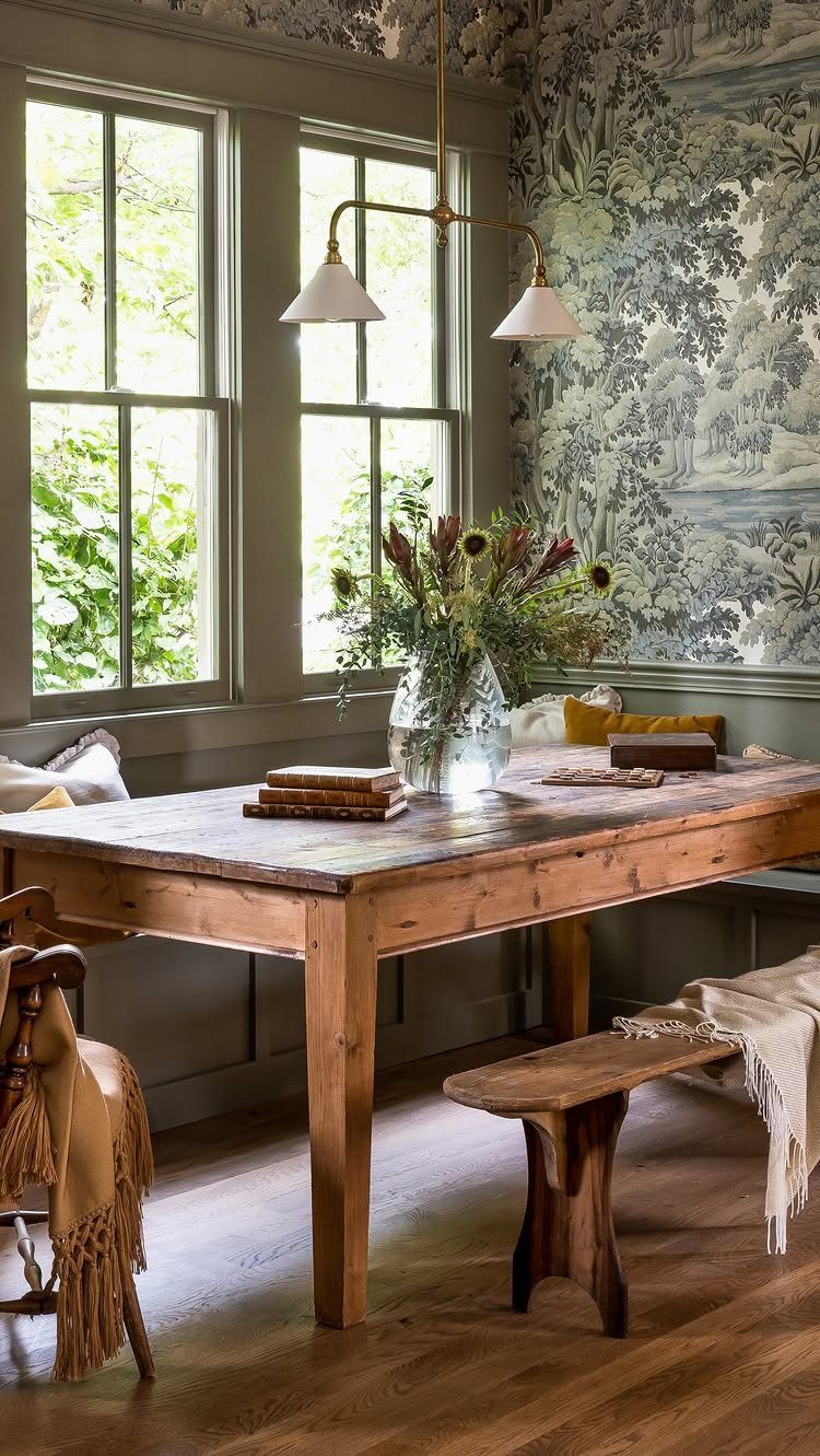 Wooden dining table with built-in banquette seating and scenic wallpaper in a rustic room