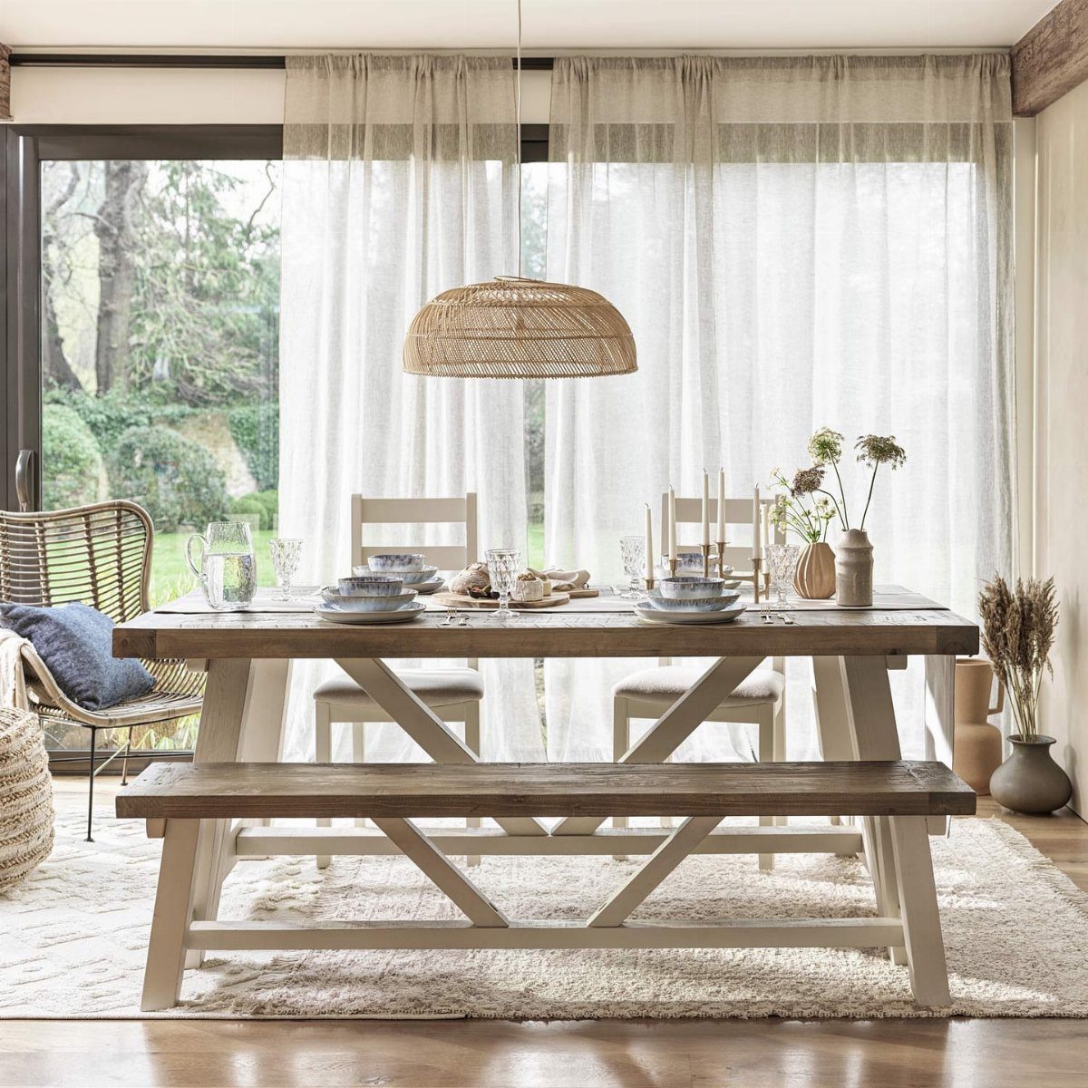 Wooden dining table with a matching bench and white chairs in a bright room.