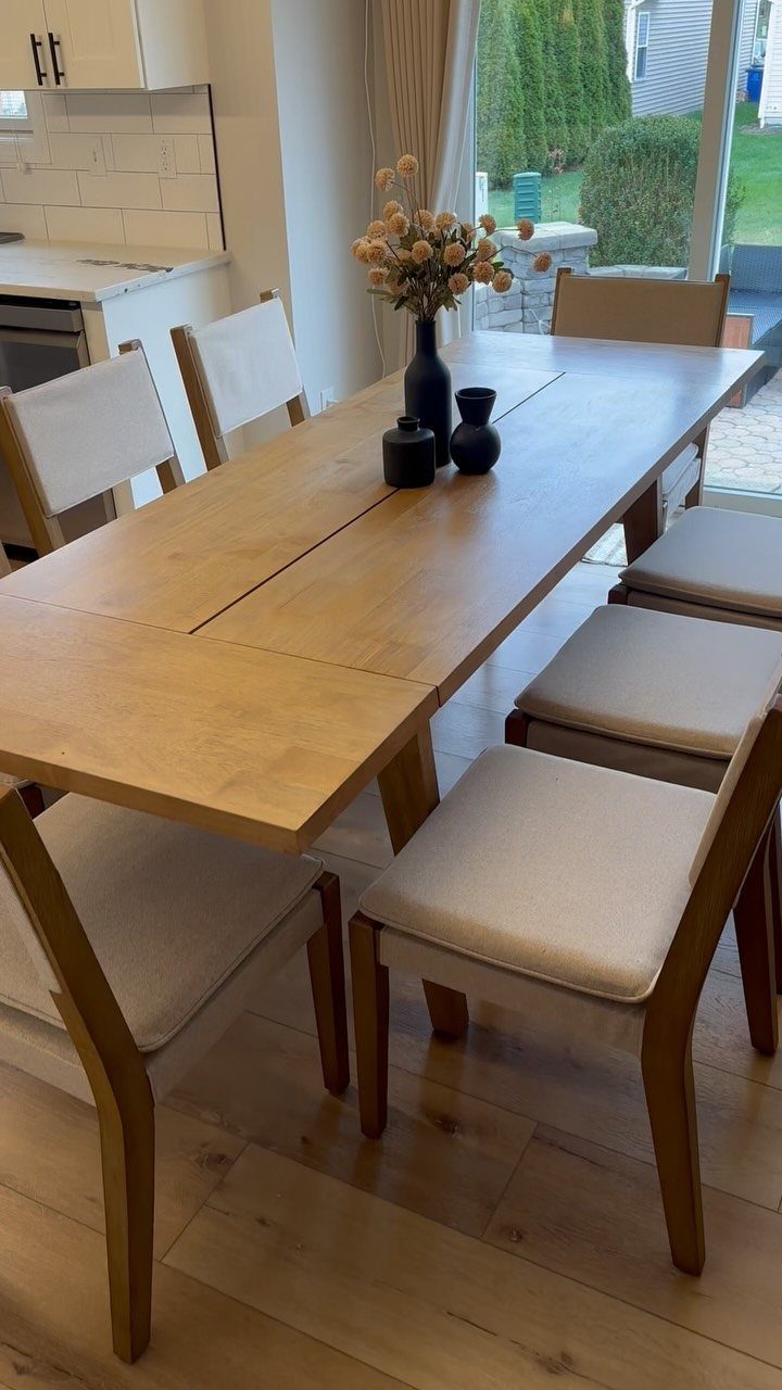 Wooden dining table with beige upholstered chairs and a black vase of flowers.
