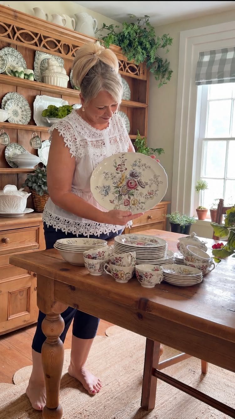 Woman holding a floral vintage plate next to a set of matching dishes.