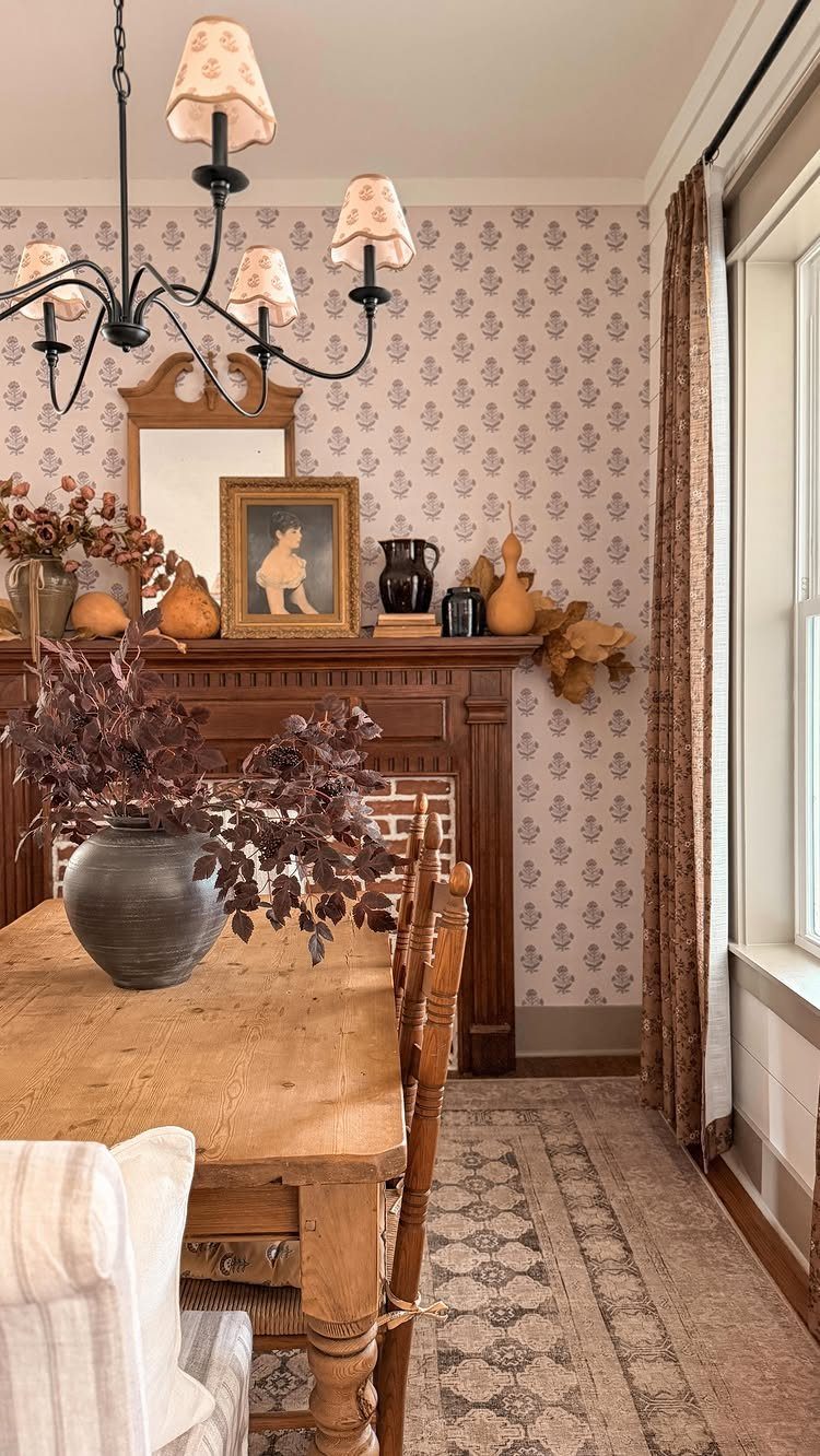 Wooden dining table and chairs in a room with floral wallpaper and fireplace.