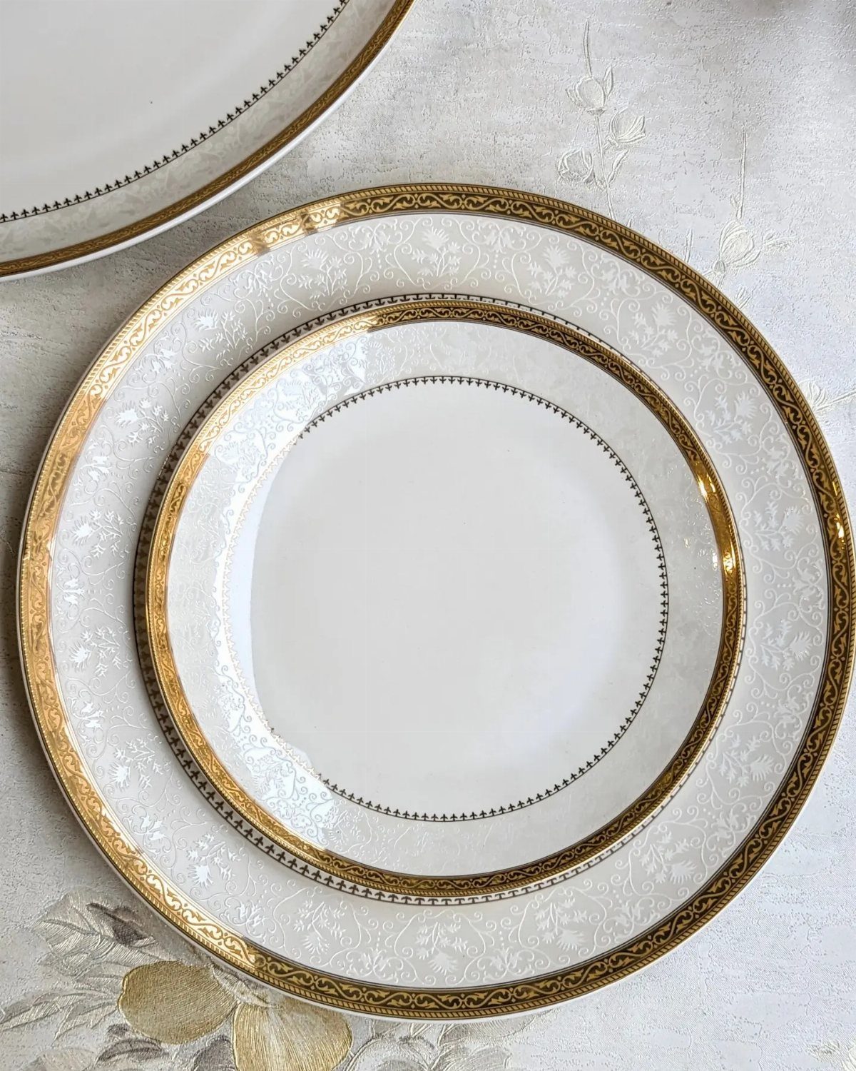 Stacked white ceramic plates with gold rims on a white textured tablecloth.