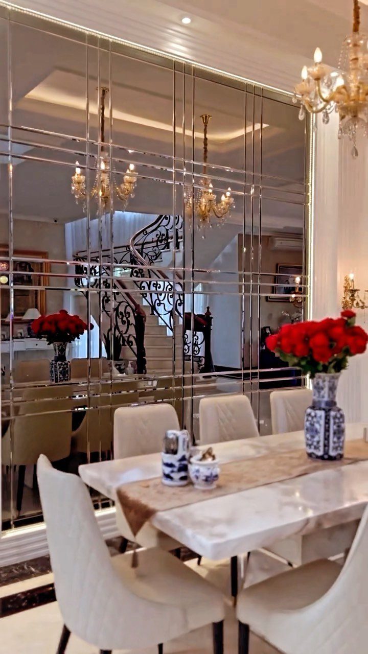 White marble dining table with red roses and mirrored wall reflecting a staircase.