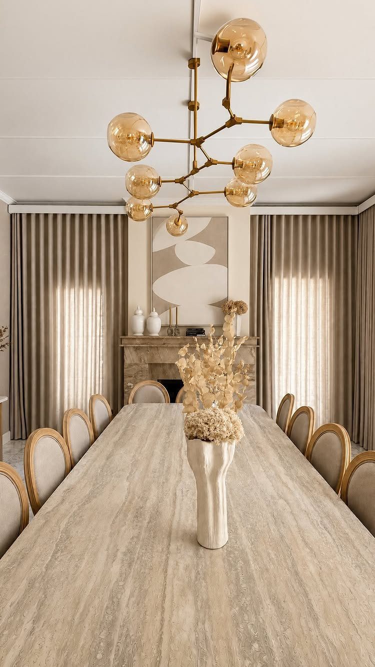 Beige marble dining table with upholstered chairs under a gold globe chandelier.