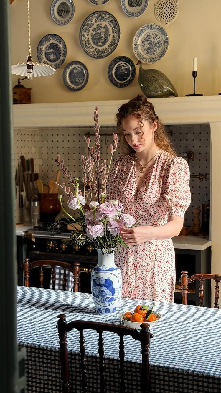 Woman arranging pink flowers in a blue and white vase on a dining table