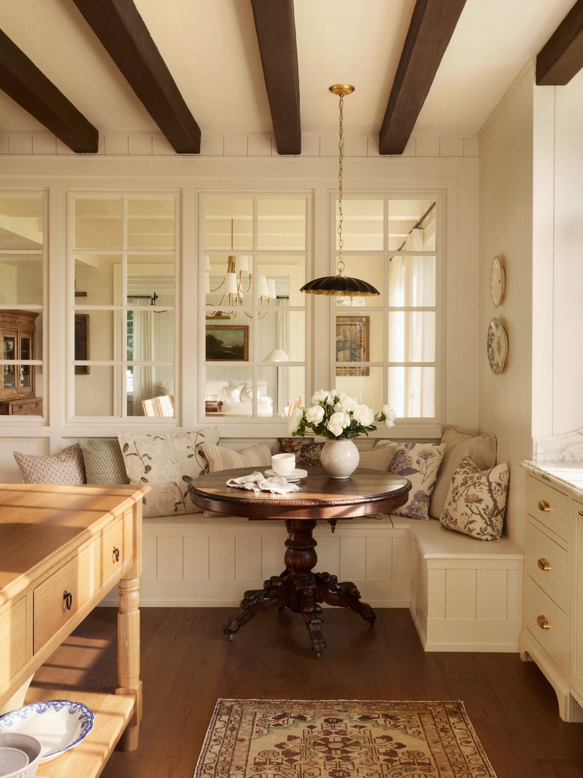 Round wooden dining table with built-in banquet seating and dark ceiling beams.