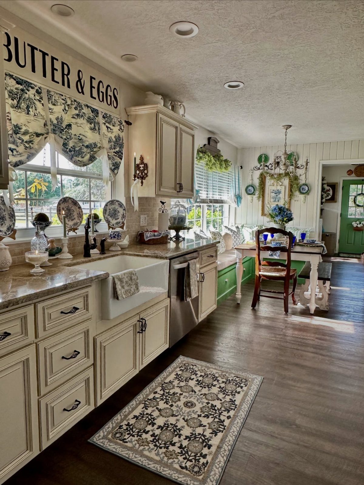 Rustic kitchen and dining area with patterned rug, floral valance, and farmhouse sink.