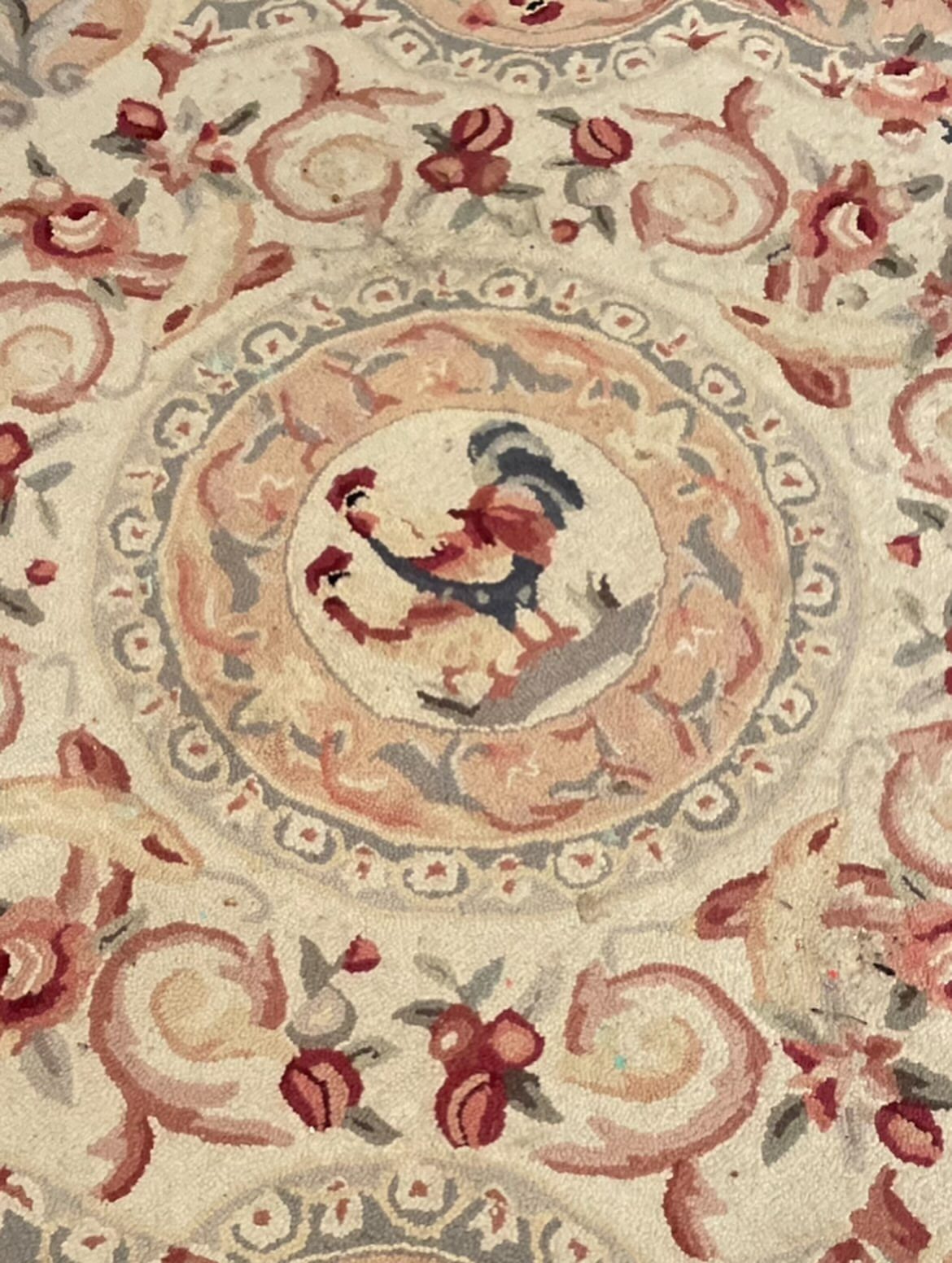 Cream woven rug with a central rooster medallion and red floral patterns.