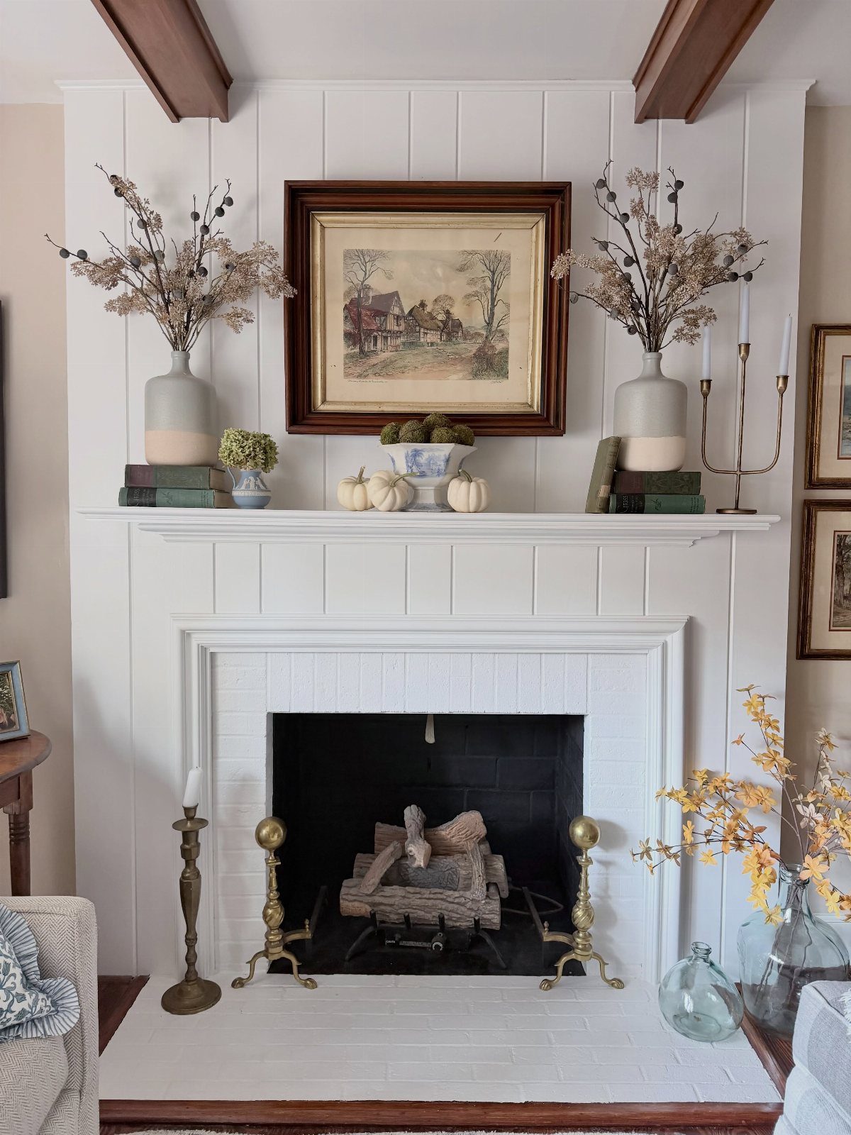 White fireplace mantel decorated with autumn pumpkins, dried branches, and a framed painting.