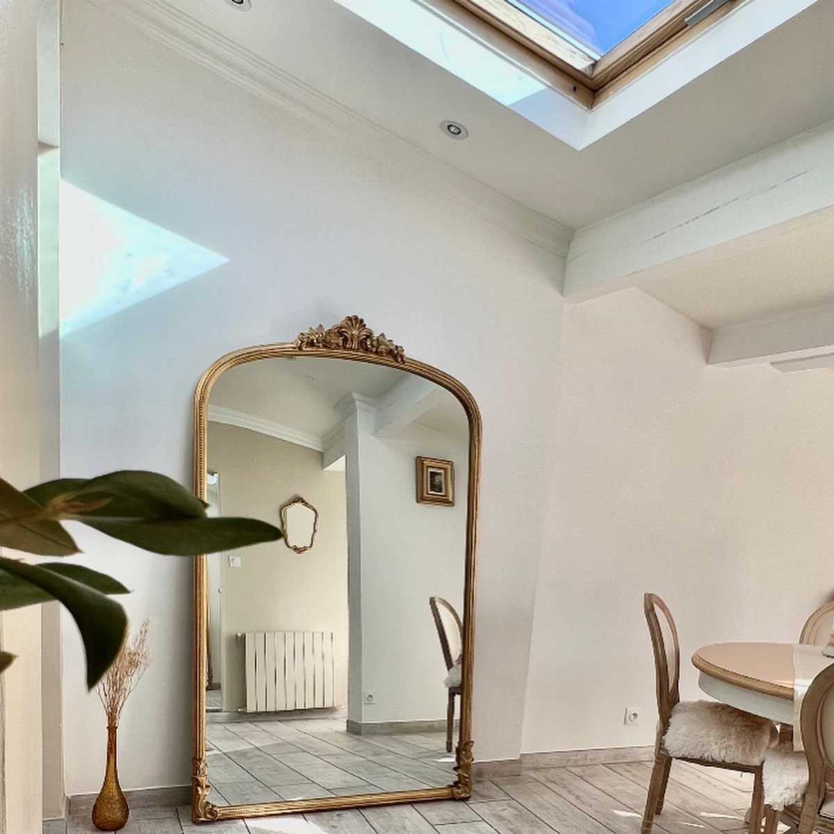 Gold-framed arched mirror leaning against a white wall in a bright dining area.