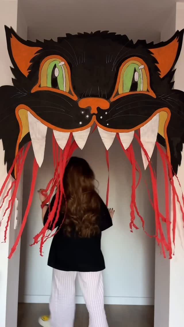 Large black cat face doorway decoration with red streamers and a person standing before it