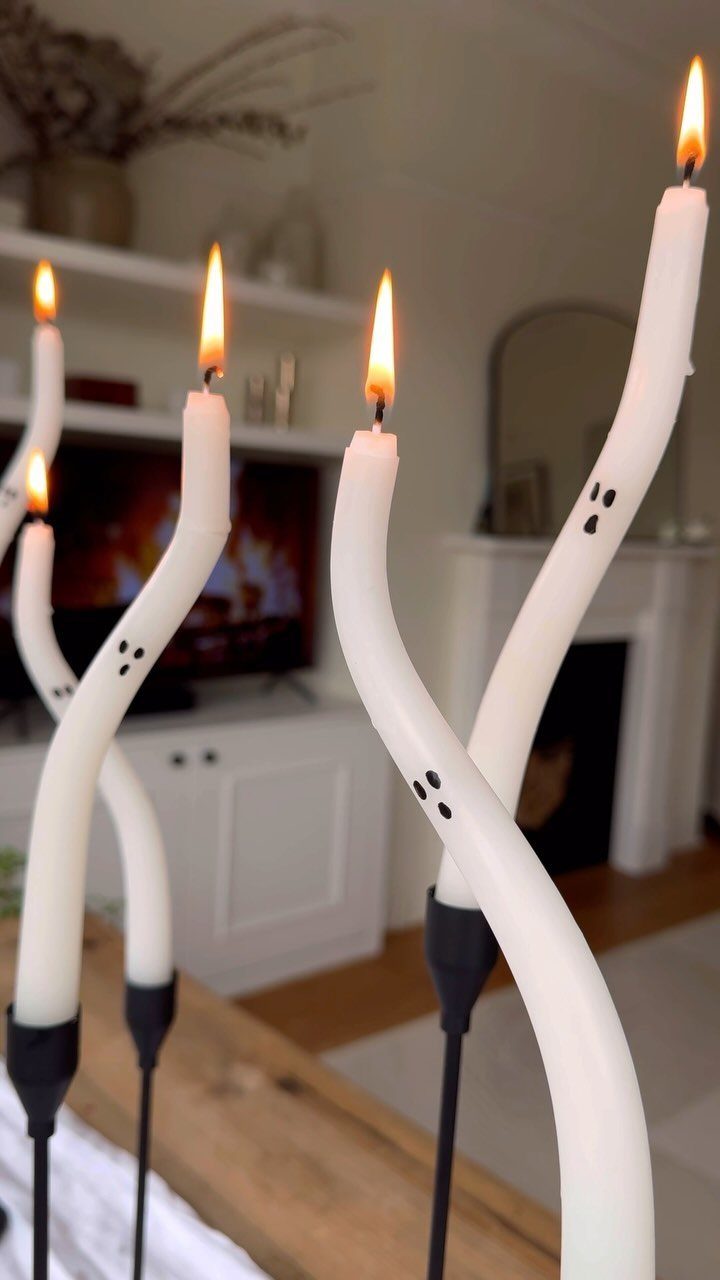 Twisted white taper candles decorated as ghosts with black faces and lit flames.