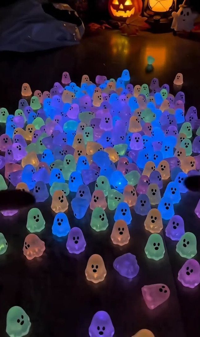 Colorful glowing ghost tea lights scattered on a dark surface with a pumpkin background