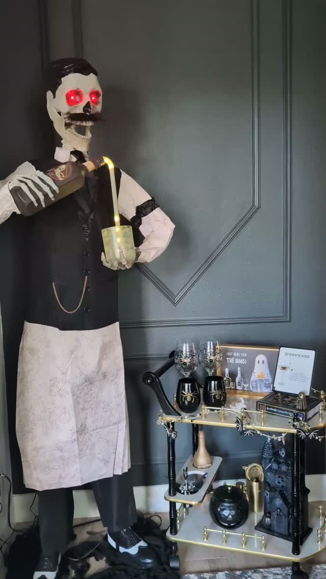 Skeleton butler standing next to a gold-trimmed gothic bar cart with spooky accessories