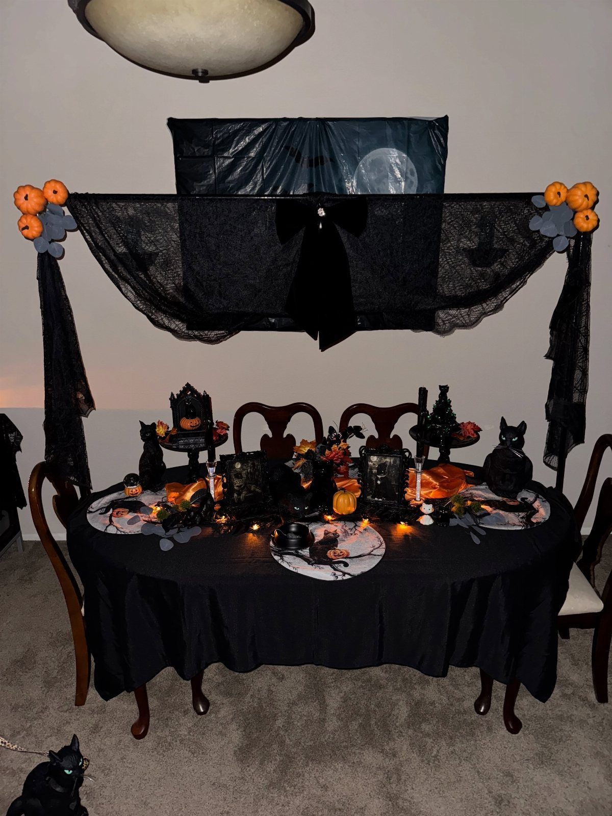 Halloween dining table with black cloth, orange pumpkins, and black cat figurines