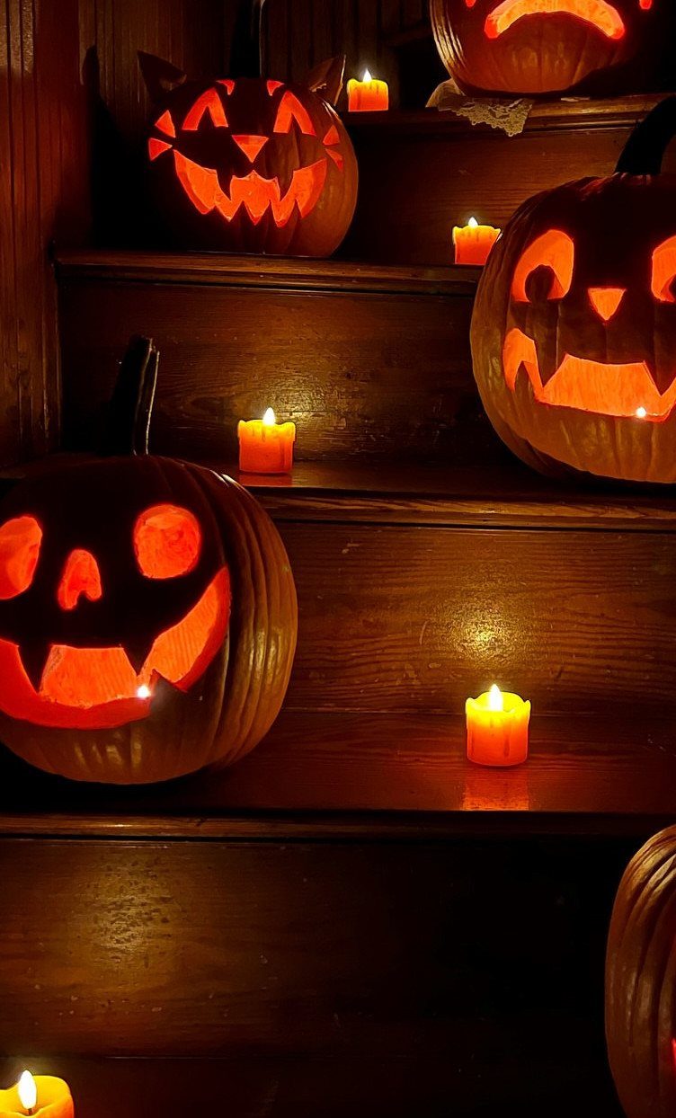 Carved glowing jack-o'-lanterns and orange candles arranged on dark wooden stairs.